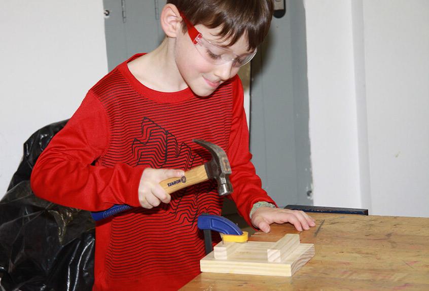 Lower school student learning to safely hammer nails